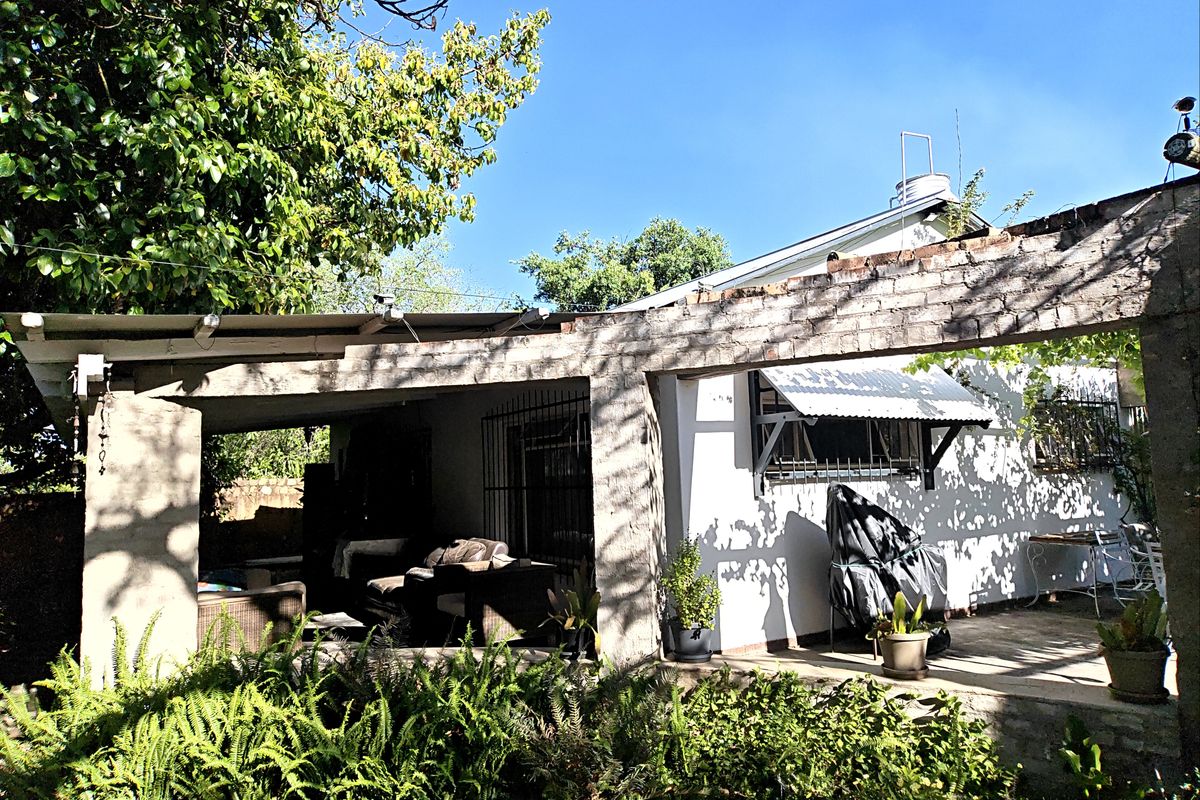 Rear exterior view featuring a covered patio area with a brick pergola structure, security bars on windows, and established garden surroundings.