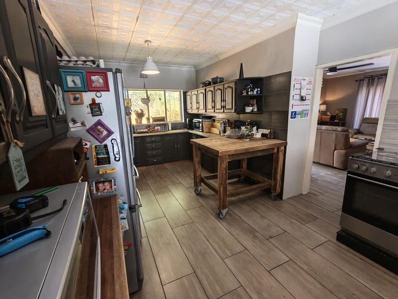A functional kitchen featuring dark cabinetry, wood-look tiled flooring, a textured ceiling, and a built-in oven, with an open-plan flow to the living area.
