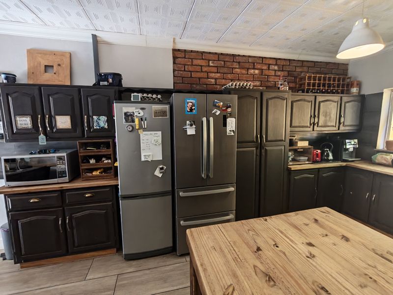 A kitchen featuring dark cabinetry, an exposed brick feature wall, tiled flooring, and a textured ceiling, providing a rustic and functional cooking space.