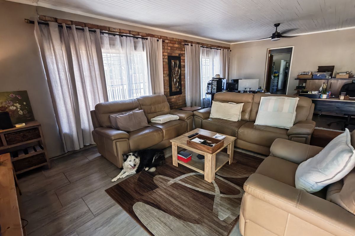 Spacious living room featuring exposed brick accent wall, tiled flooring, and timber-look ceiling panels with an integrated ceiling fan.
