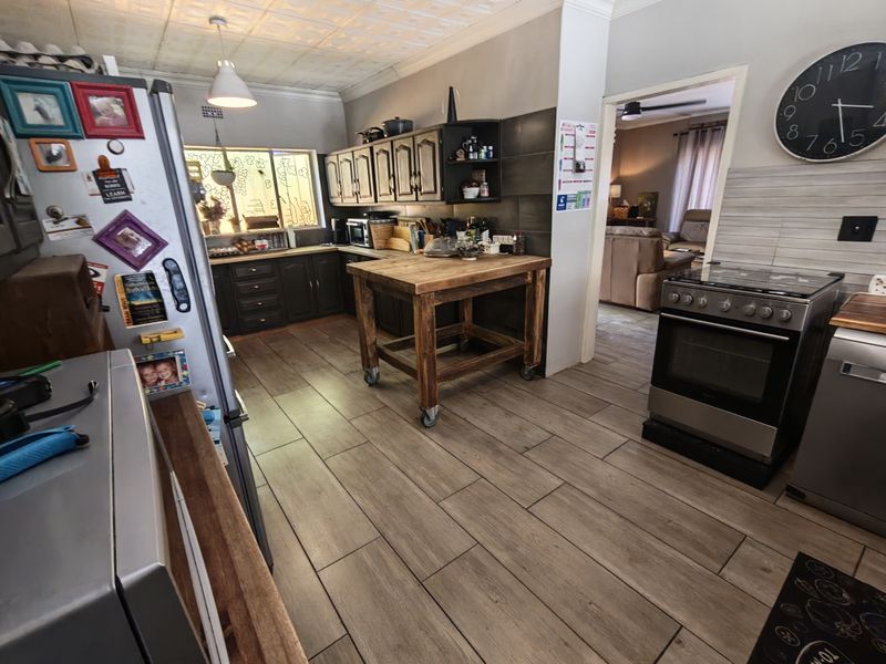 A functional kitchen featuring dark cabinetry, wood-look tiled flooring, a freestanding stove, and a central wooden prep island with a tiled backsplash.