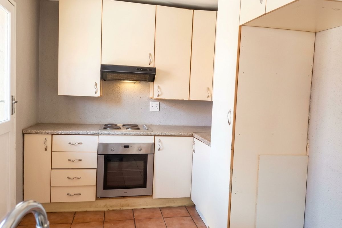 A functional kitchen featuring built-in cabinetry, an electric hob, an oven, and tiled flooring, offering a blank canvas for potential modern updates.