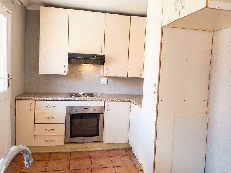 A functional kitchen featuring built-in cabinetry, an electric hob, an oven, and tiled flooring, offering a blank canvas for potential modern updates.