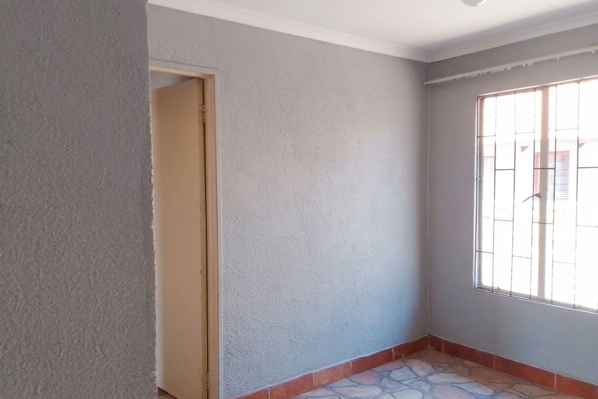 An empty bedroom featuring grey textured walls, tiled flooring, and a window fitted with security bars.