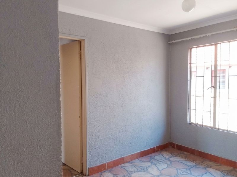 An empty bedroom featuring grey textured walls, tiled flooring, and a window fitted with security bars.