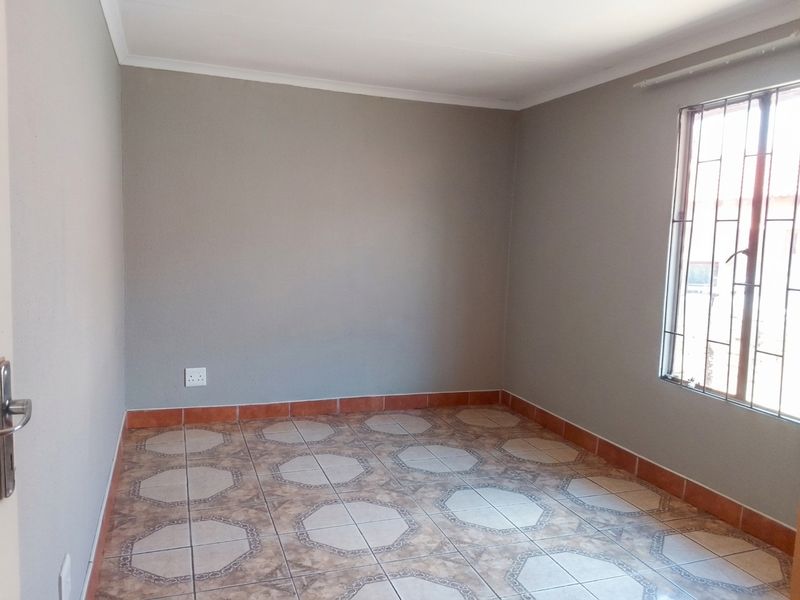 An empty bedroom featuring neutral grey walls, patterned ceramic floor tiles, and a window fitted with security bars.