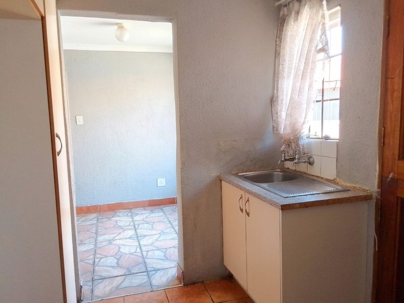 A compact scullery area featuring a stainless steel sink, built-in cabinetry, and tiled flooring, providing a functional utility space adjacent to the main room.
