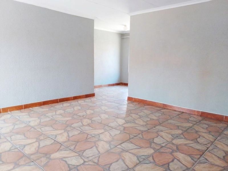 An empty, open-plan living area featuring neutral grey walls, patterned ceramic tile flooring, and coved ceilings, offering a blank canvas for interior design.