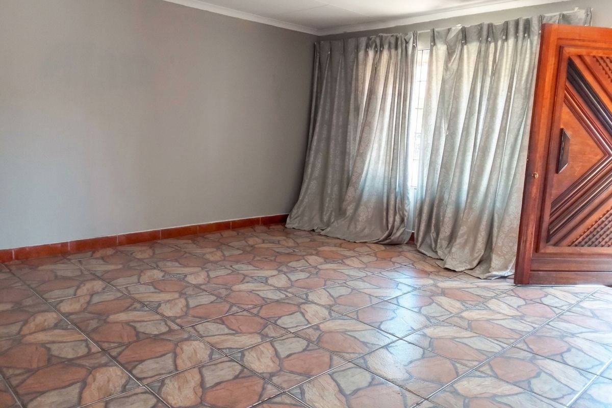 An empty living room featuring patterned ceramic floor tiles, neutral grey walls, and a solid wooden entrance door.