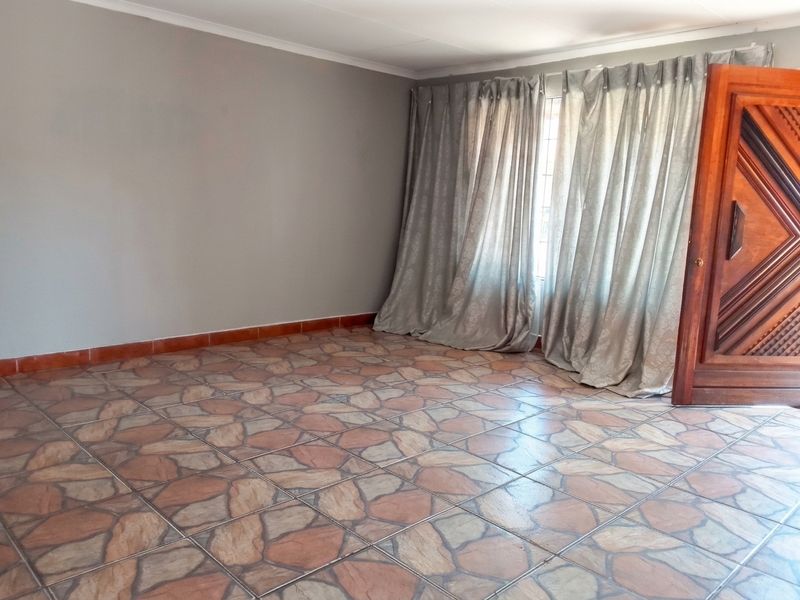 An empty living room featuring patterned ceramic floor tiles, neutral grey walls, and a solid wooden entrance door.