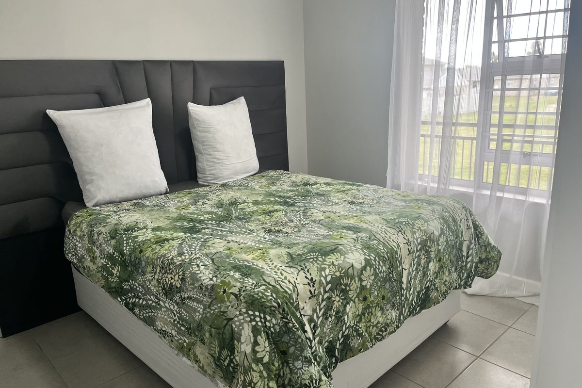 A well-lit bedroom featuring neutral tiled flooring and a window fitted with security bars, providing a clean and functional living space.