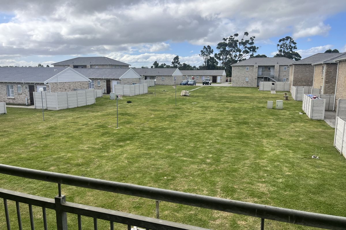 Elevated view overlooking a spacious communal garden area within a residential apartment complex, featuring well-maintained lawns and surrounding brick apartment buildings.