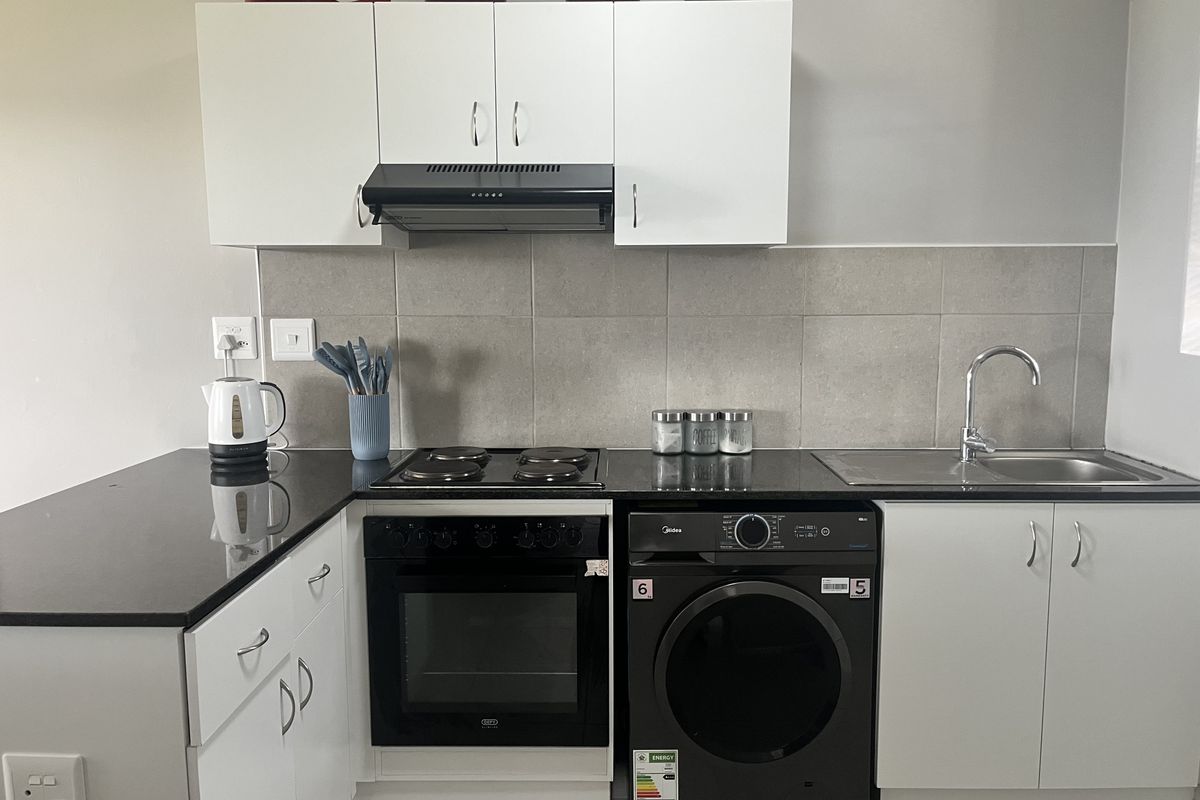 A functional kitchen featuring white cabinetry, black granite countertops, a tiled splashback, and integrated appliances including an oven, hob, and extractor fan.