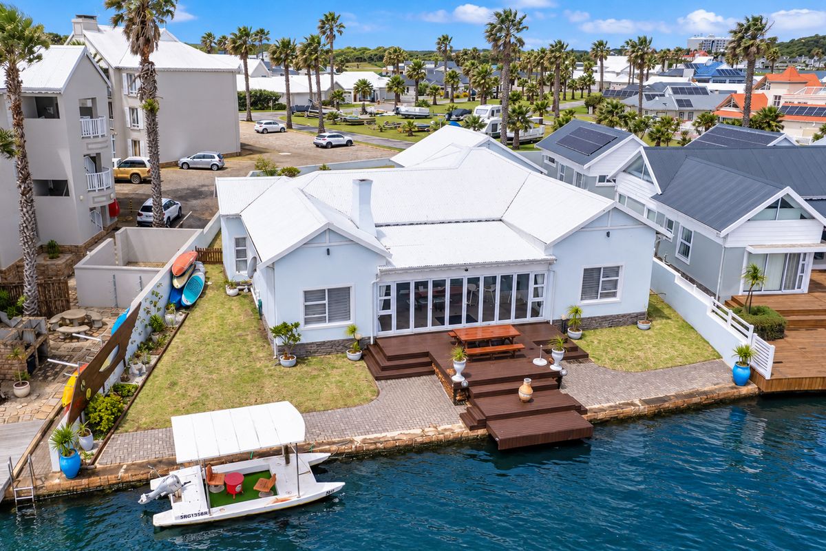 Aerial view of a waterfront property featuring a white facade, timber decking, paved patio area, and private jetty access to the canal.
