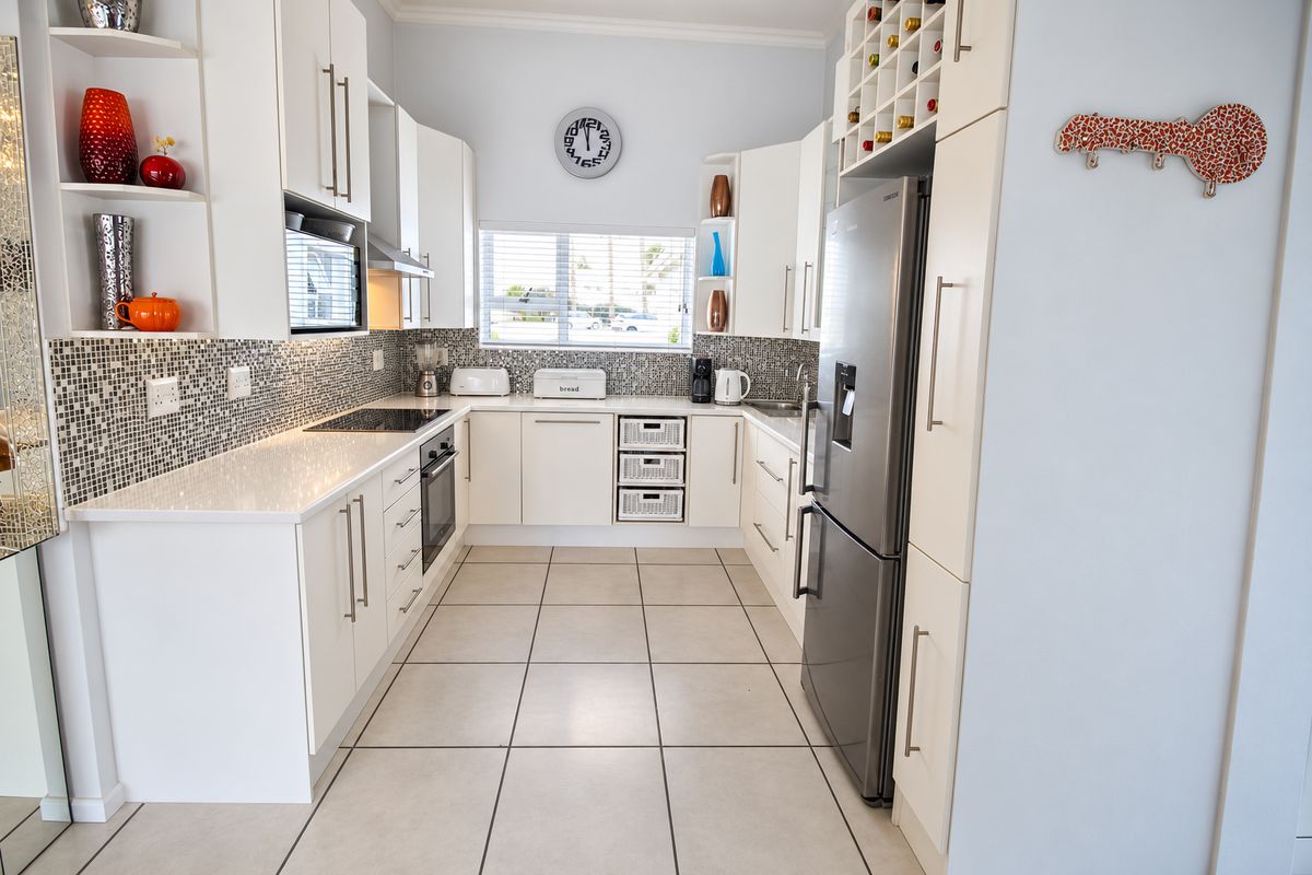 Modern U-shaped kitchen featuring white cabinetry, stone countertops, mosaic tile backsplash, and integrated appliances with neutral ceramic floor tiling.