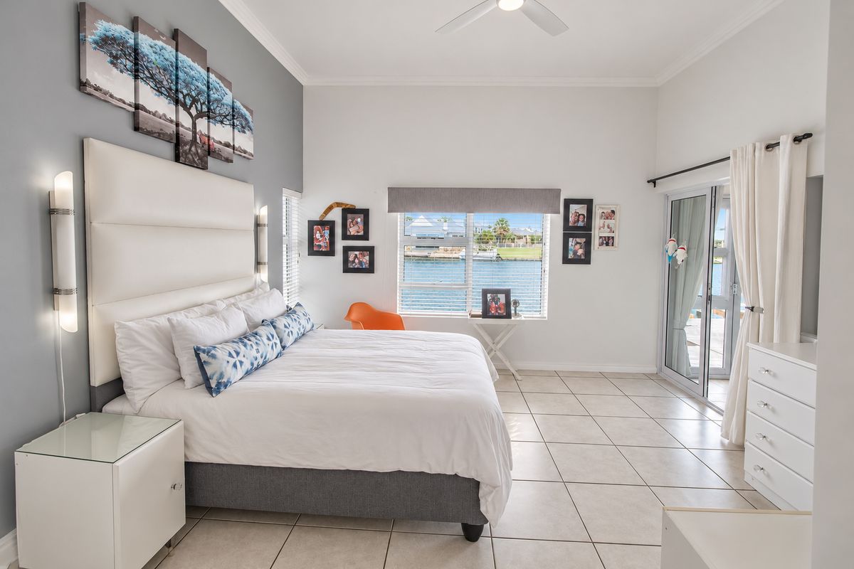 Spacious bedroom featuring tiled flooring, a ceiling fan, and large sliding glass doors providing natural light and views of the water.