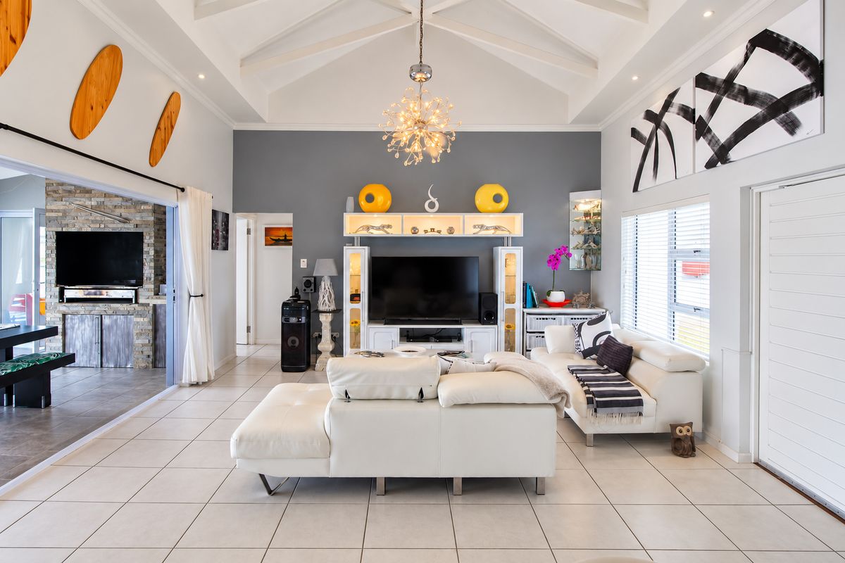 Spacious living room featuring a high vaulted ceiling with exposed beams, tiled flooring, and large sliding doors opening to an adjacent patio area.