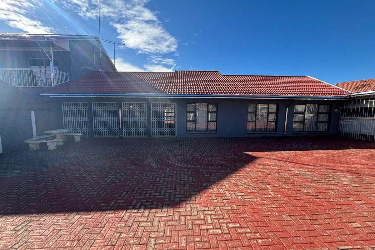 A spacious rear courtyard featuring extensive red brick paving, a tiled roof structure, and secure access points with metal security gates and window frames.