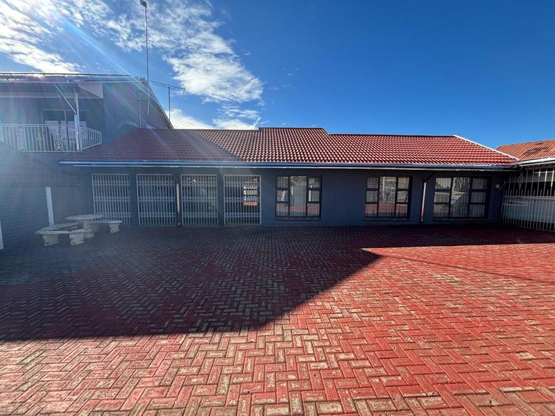 A spacious rear courtyard featuring extensive red brick paving, a tiled roof structure, and secure access points with metal security gates and window frames.