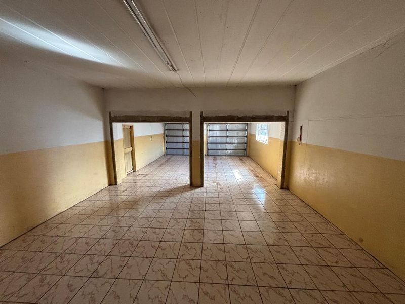 A spacious, empty double garage featuring tiled flooring, dual garage doors, and basic lighting, offering significant potential for storage or workshop conversion.