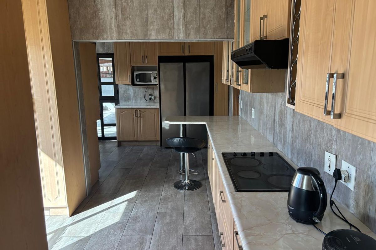 A functional kitchen featuring light wood cabinetry, laminate countertops, an integrated hob with extractor fan, and tiled flooring with a breakfast bar area.