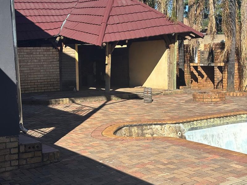 Outdoor pool area featuring brick paving, a covered patio structure, and a built-in braai, requiring maintenance and cosmetic updates.