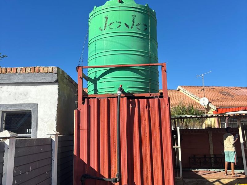 An exterior view of a water storage tank mounted on a raised metal support structure in the rear yard area.