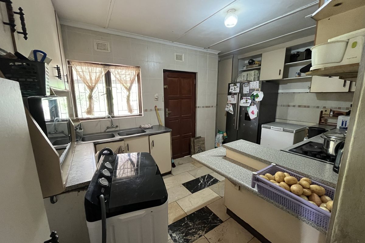 A functional kitchen featuring built-in cabinetry, a double basin sink, breakfast counter, and tiled finishes throughout, offering potential for modernization.