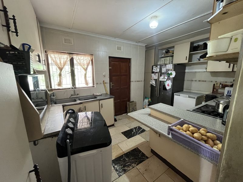 A functional kitchen featuring built-in cabinetry, a double basin sink, breakfast counter, and tiled finishes throughout, offering potential for modernization.