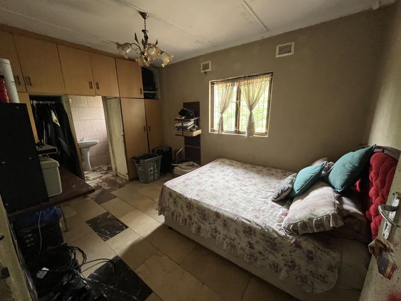 Bedroom featuring built-in cupboards, tiled flooring, and an en-suite bathroom area. The room requires cosmetic updates to improve its overall condition.