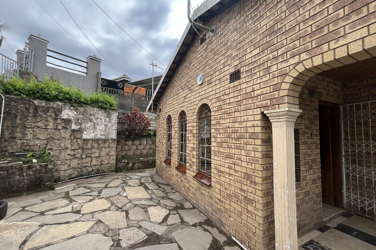 Rear exterior view featuring a face brick facade, arched windows, and a stone-paved patio area with a retaining wall.