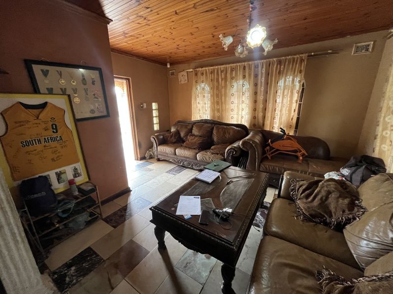 A living room featuring a timber-clad ceiling, tiled flooring, and a glass block accent wall, offering a dated aesthetic ready for modernization.