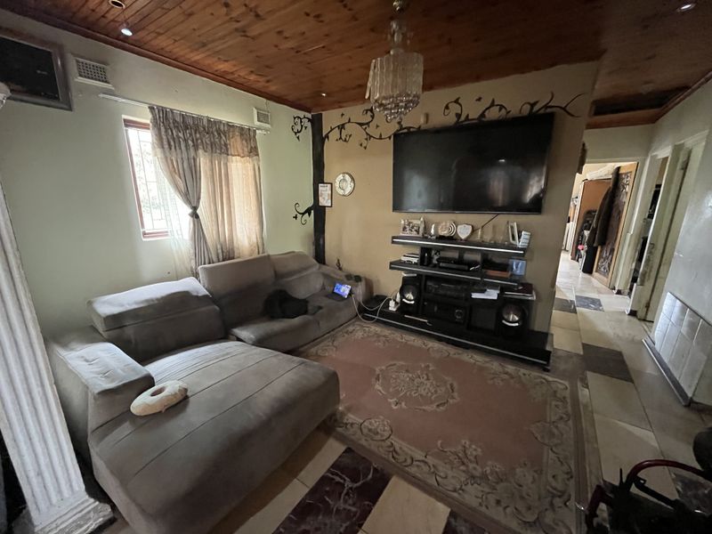 Living room featuring a timber-clad ceiling, tiled flooring, and a decorative wall mural, providing a functional space with potential for modern updates.