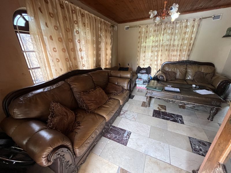 A living room featuring a timber ceiling, stone tile flooring with decorative inlays, and an arched window.