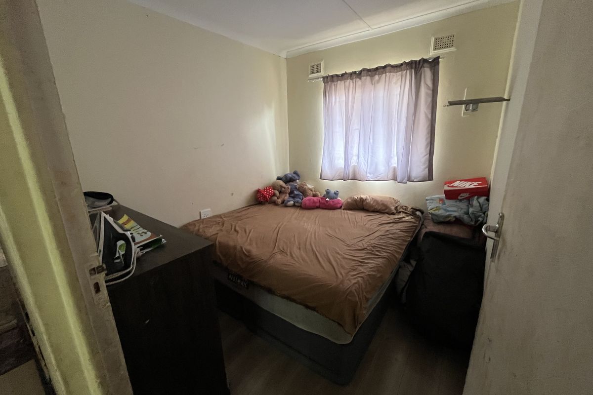 A compact bedroom featuring laminate flooring and a window with ventilation grilles, requiring minor cosmetic updates to improve its overall appeal.