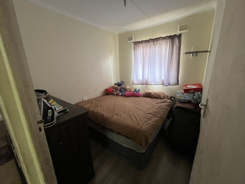 A compact bedroom featuring laminate flooring and a window with ventilation grilles, requiring minor cosmetic updates to improve its overall appeal.