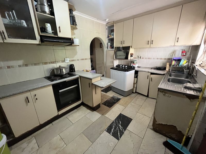 A functional kitchen featuring built-in cabinetry, laminate countertops, an integrated oven and hob, and a double stainless steel sink with tiled splashbacks.