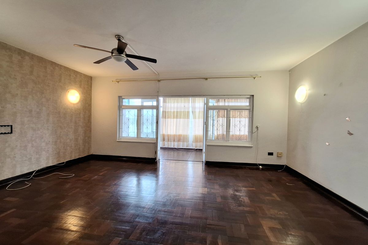 Spacious living room featuring original parquet flooring, a ceiling fan, and sliding glass doors leading to an enclosed balcony area.