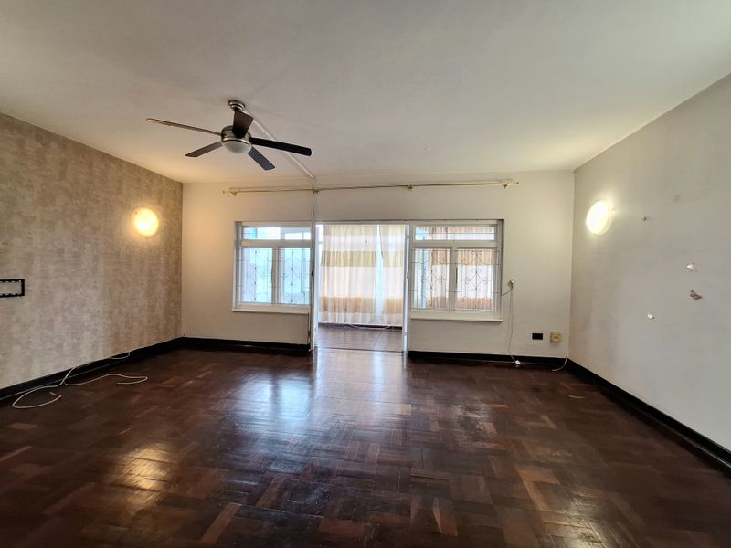 Spacious living room featuring original parquet flooring, a ceiling fan, and sliding glass doors leading to an enclosed balcony area.