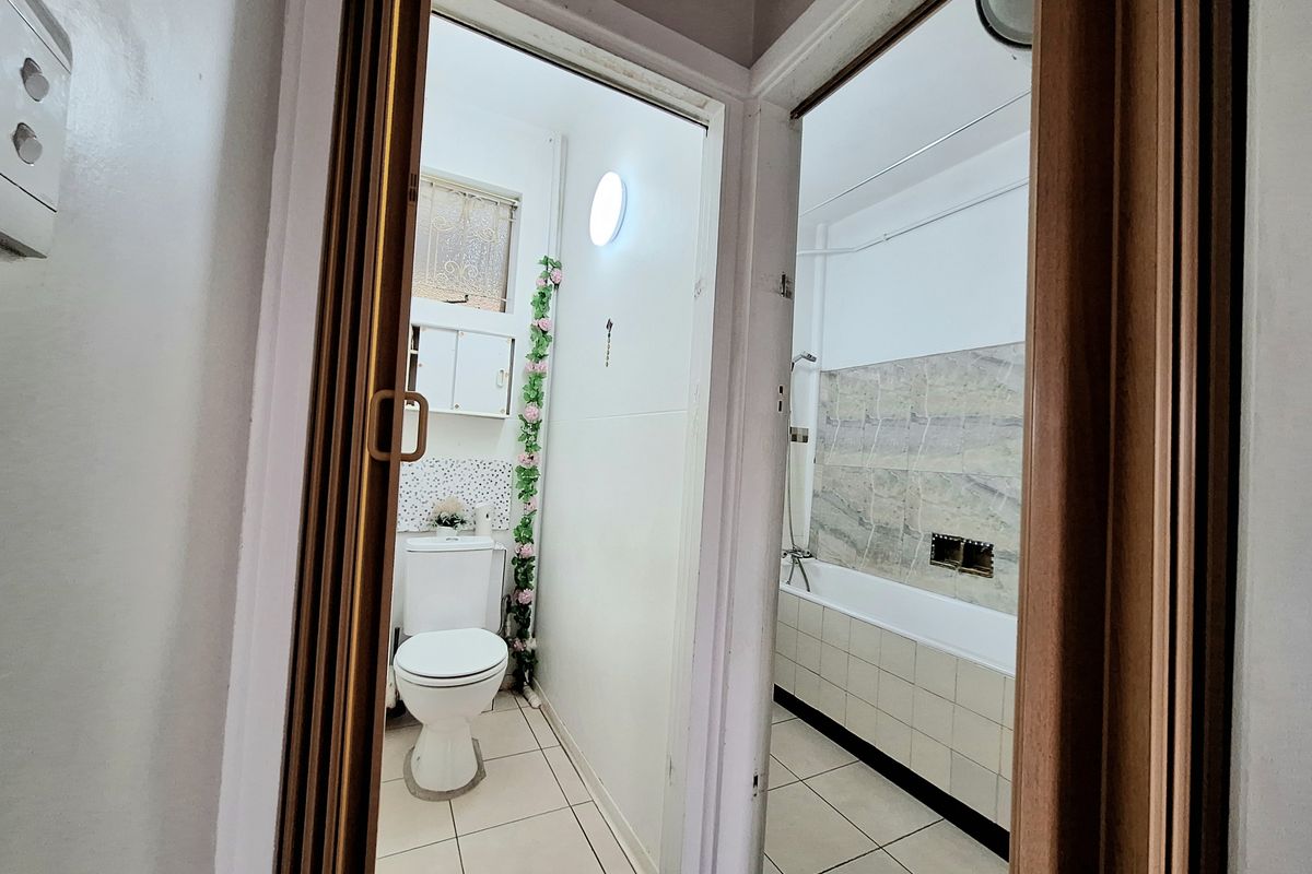 A functional bathroom featuring a toilet, bathtub with shower mixer, and tiled finishes, viewed through a doorway.