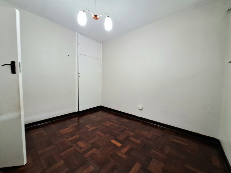 An empty bedroom featuring classic parquet flooring, neutral walls, and a built-in cupboard, offering a clean and versatile space ready for personalization.