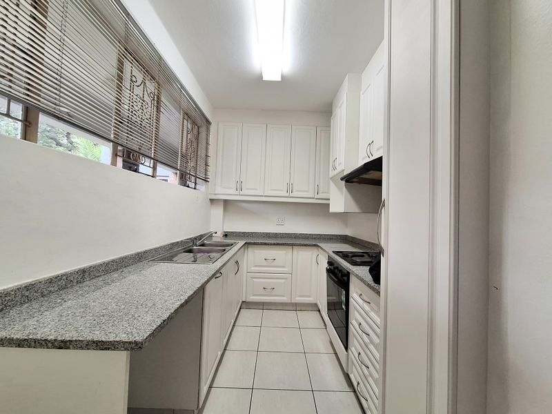 A clean, functional galley-style kitchen featuring white cabinetry, granite countertops, a double basin sink, and built-in cooking appliances.