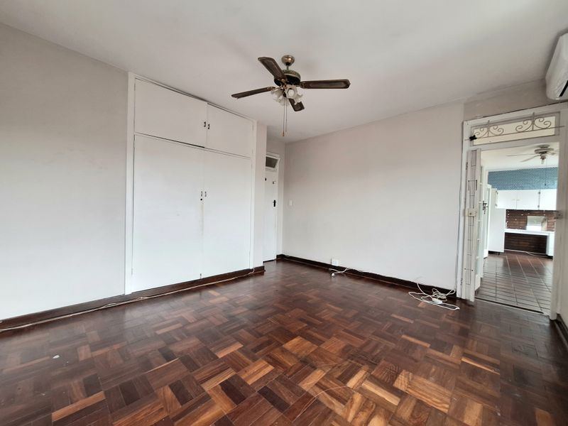 Spacious bedroom featuring classic parquet flooring, built-in storage cupboards, and a ceiling fan, offering a blank canvas for personalization.