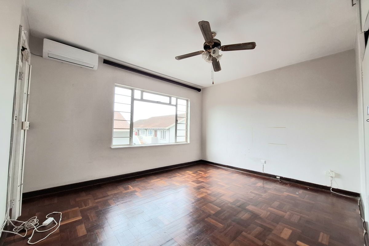 An empty bedroom featuring classic parquet flooring, a ceiling fan, and a wall-mounted air conditioning unit.
