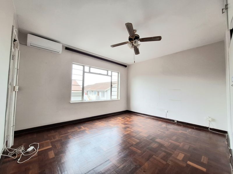An empty bedroom featuring classic parquet flooring, a ceiling fan, and a wall-mounted air conditioning unit.