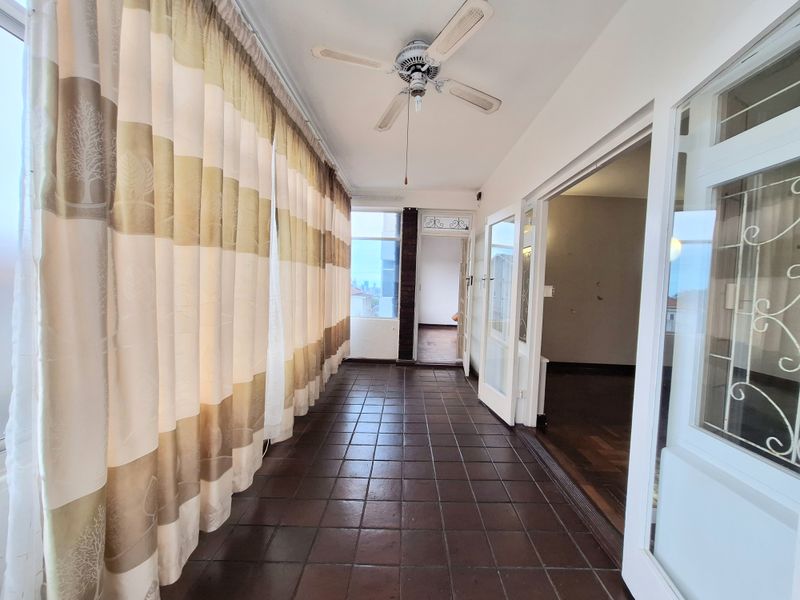 An enclosed balcony or sunroom featuring tiled flooring, a ceiling fan, and large windows, providing a bright transition space between the interior and exterior.
