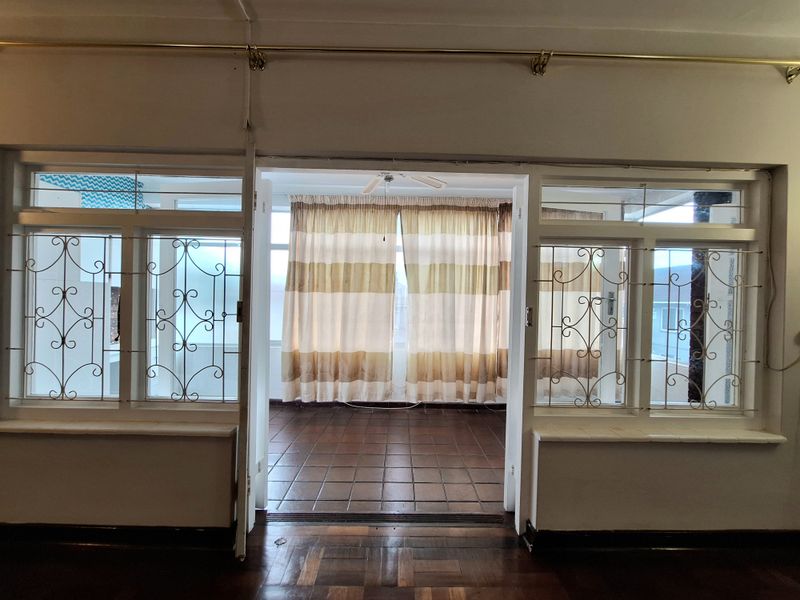 Spacious living area featuring parquet flooring, tiled transition space, and large windows with security bars, offering a bright and open layout.