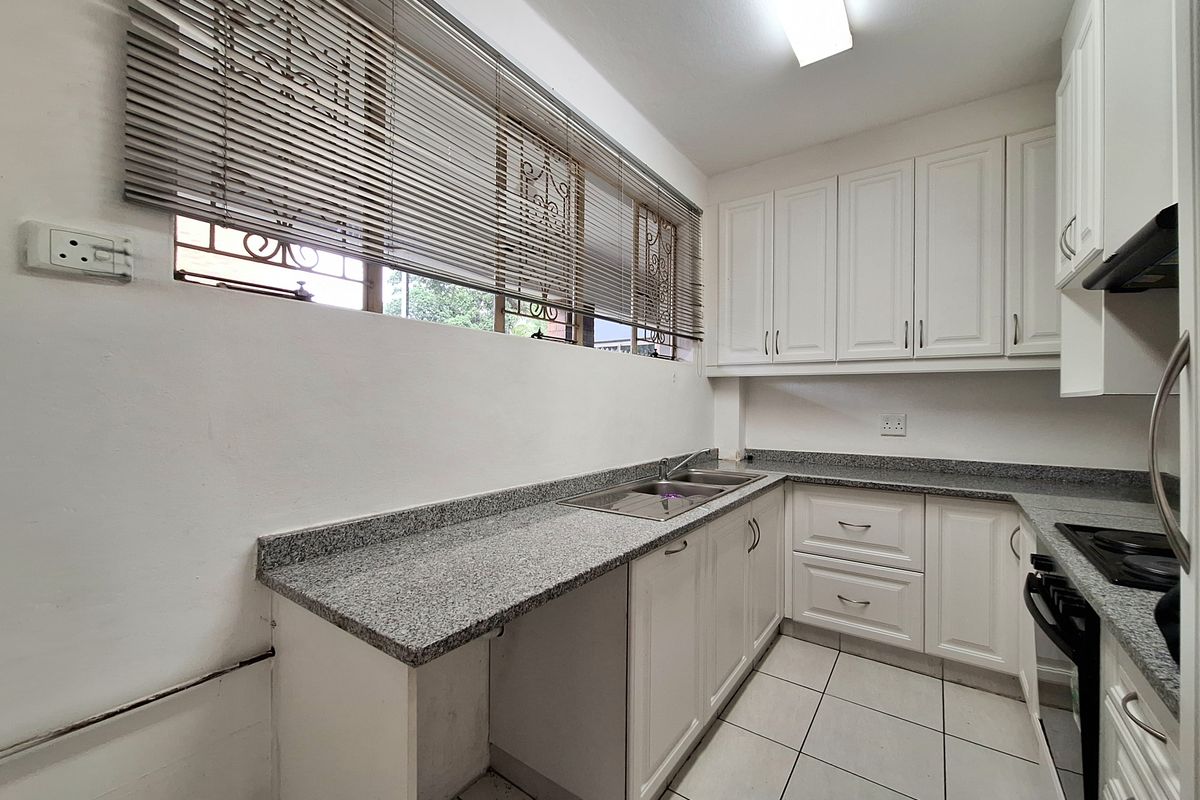A functional kitchen featuring white cabinetry, granite countertops, a stainless steel double sink, and a built-in hob with an extractor fan.