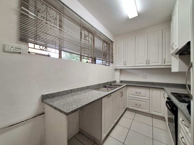 A functional kitchen featuring white cabinetry, granite countertops, a stainless steel double sink, and a built-in hob with an extractor fan.