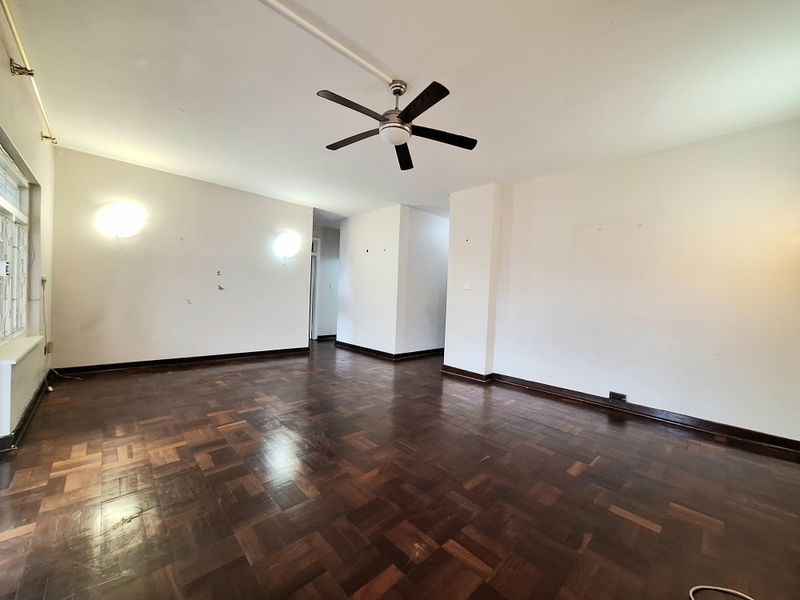 Spacious living area featuring original parquet flooring, a ceiling fan, and wall-mounted lighting, presenting a blank canvas for interior design.